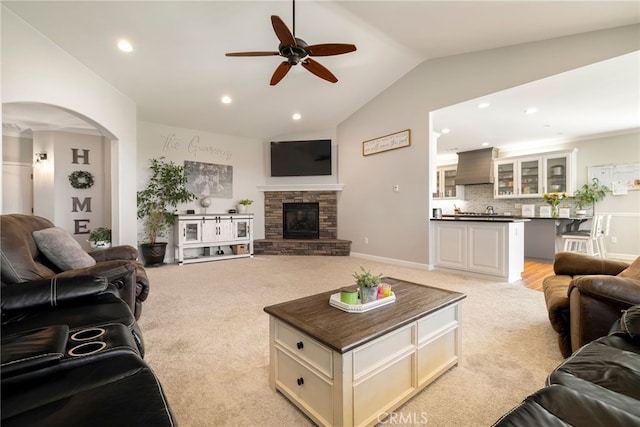 living room featuring a fireplace, arched walkways, vaulted ceiling, and light colored carpet