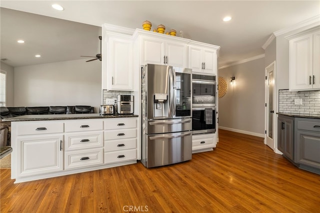 kitchen with appliances with stainless steel finishes, white cabinets, light wood finished floors, and decorative backsplash