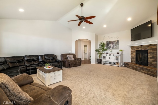 carpeted living room featuring arched walkways, recessed lighting, a ceiling fan, vaulted ceiling, and a stone fireplace