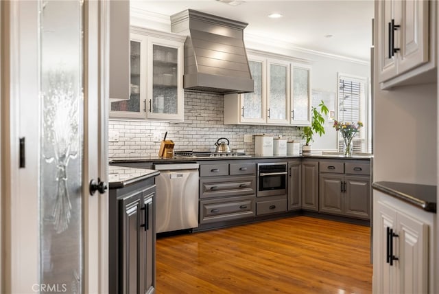 kitchen featuring crown molding, custom range hood, decorative backsplash, appliances with stainless steel finishes, and wood finished floors