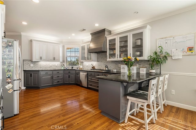 kitchen featuring gray cabinetry, appliances with stainless steel finishes, wood finished floors, premium range hood, and a peninsula