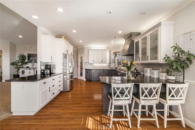 kitchen with freestanding refrigerator, dark wood-style flooring, a peninsula, and wall chimney exhaust hood