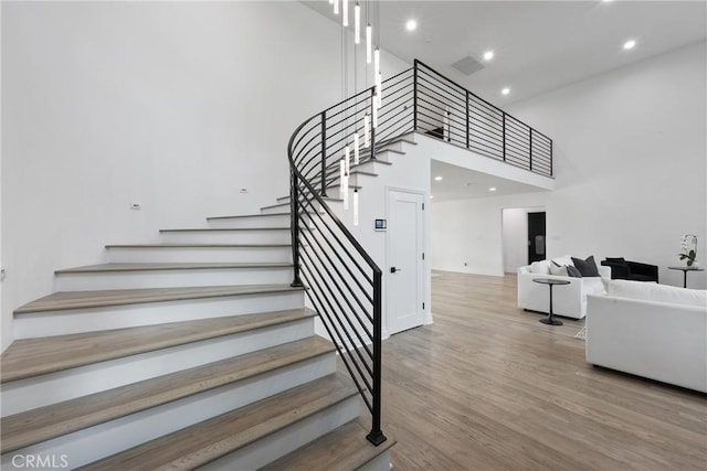 stairs with a towering ceiling, visible vents, wood finished floors, and recessed lighting