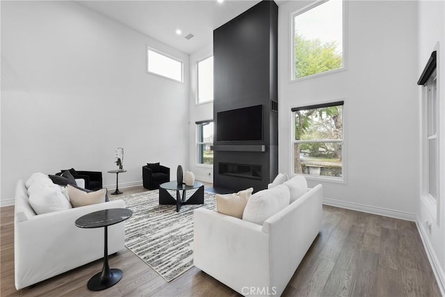 living room featuring a glass covered fireplace, wood finished floors, a towering ceiling, and baseboards