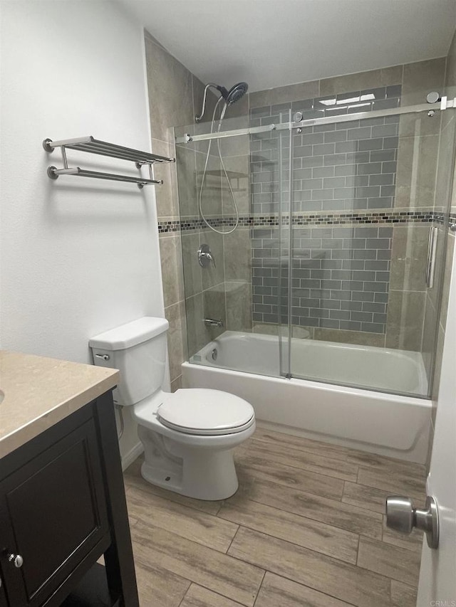 bathroom featuring wood finish floors, vanity, toilet, and bath / shower combo with glass door