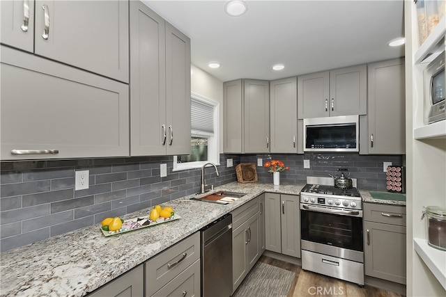 kitchen featuring tasteful backsplash, stainless steel appliances, a sink, and gray cabinetry