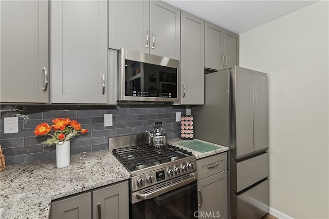 kitchen featuring stainless steel appliances, gray cabinets, light stone counters, and tasteful backsplash