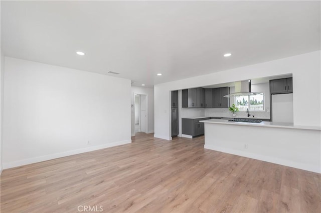 kitchen featuring recessed lighting, light countertops, wall chimney range hood, and light wood finished floors