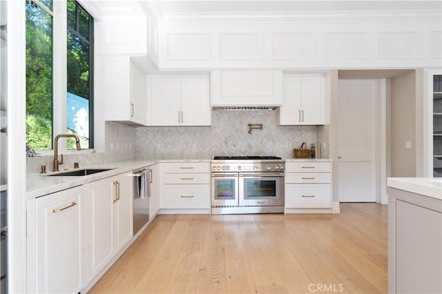 kitchen with light wood-style flooring, stainless steel appliances, a sink, light countertops, and backsplash