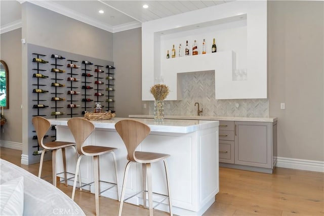 bar with baseboards, light wood-style flooring, ornamental molding, backsplash, and recessed lighting