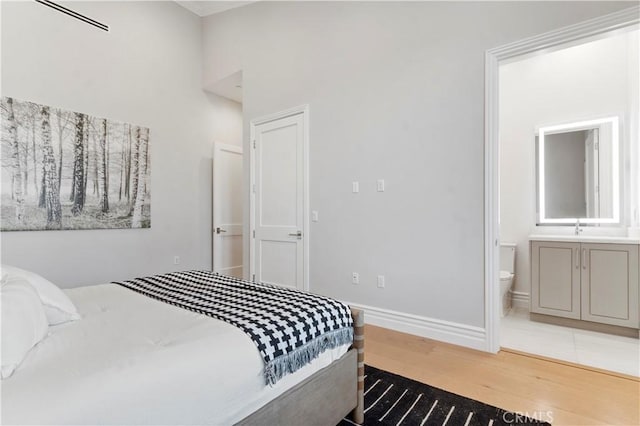 bedroom featuring a sink, baseboards, wood finished floors, and ensuite bathroom