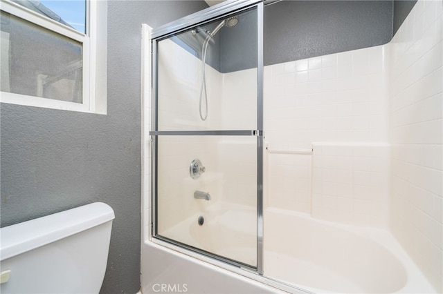 bathroom featuring toilet, shower / bath combination with glass door, and a textured wall