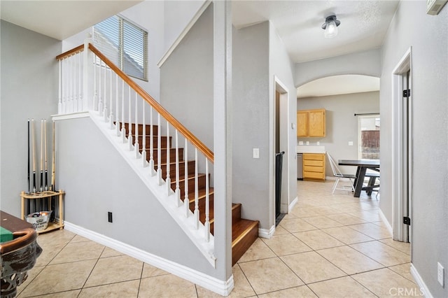 staircase with baseboards, arched walkways, and tile patterned floors