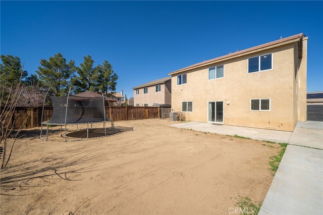 back of house featuring stucco siding, a fenced backyard, a trampoline, and a patio