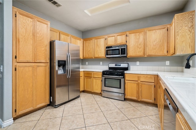 kitchen with light tile patterned floors, a sink, visible vents, appliances with stainless steel finishes, and tile counters