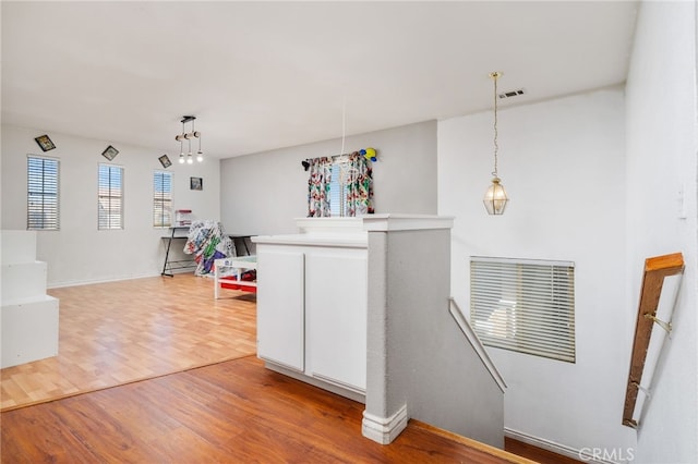 interior space featuring light wood finished floors, visible vents, white cabinets, and decorative light fixtures