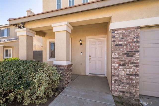 view of exterior entry featuring brick siding, an attached garage, and stucco siding