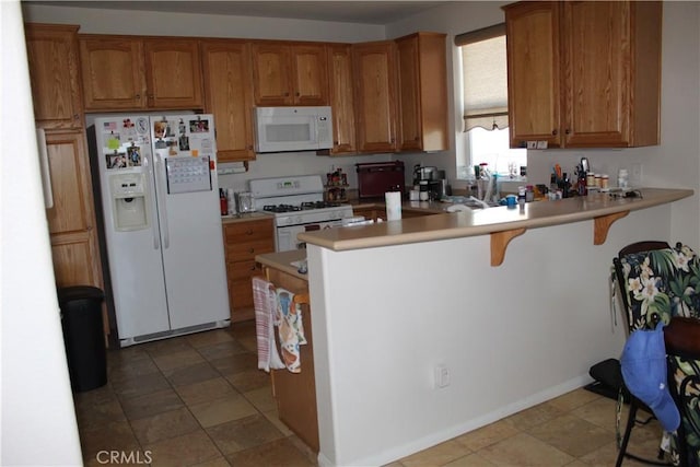 kitchen with a peninsula, white appliances, brown cabinets, and light countertops