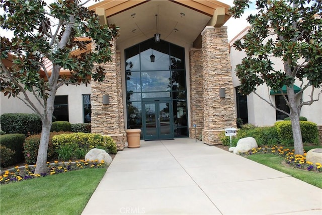 entrance to property featuring stone siding, stucco siding, and french doors