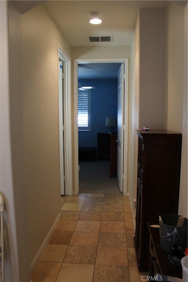 hall with stone tile floors, visible vents, and baseboards