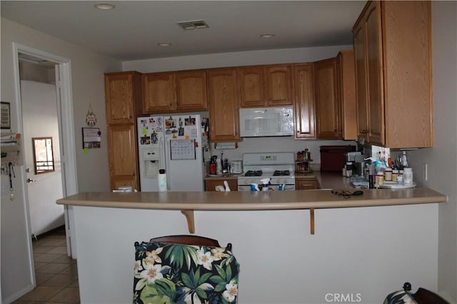 kitchen with light tile patterned floors, light countertops, brown cabinetry, white appliances, and a peninsula