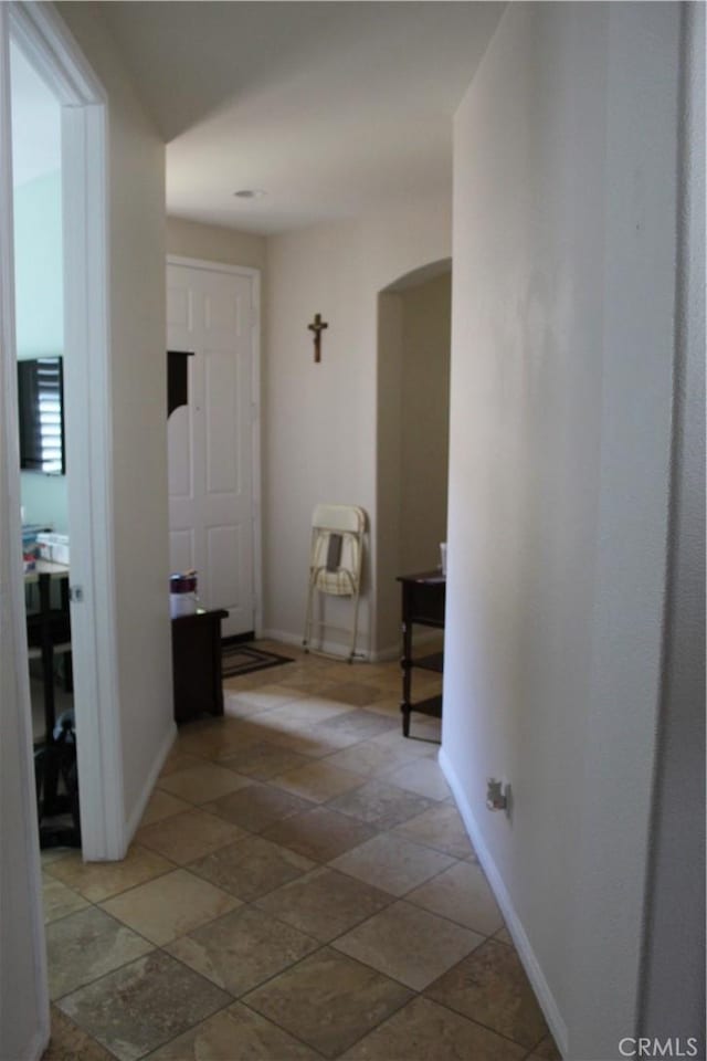 hall featuring arched walkways and baseboards