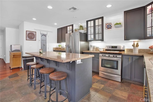 kitchen with visible vents, stone finish floor, stainless steel appliances, light stone counters, and a center island