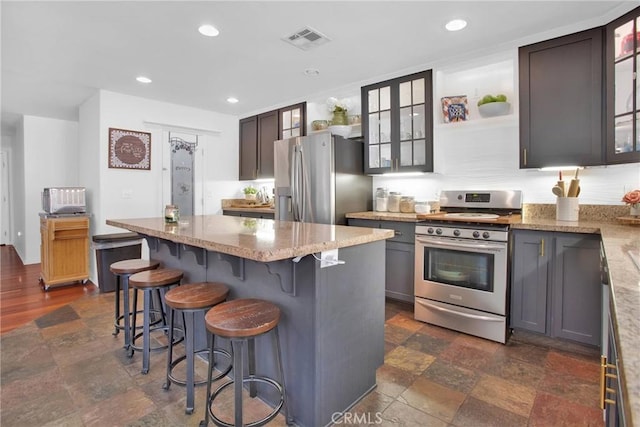 7575 Rancho Rd, Wrightwood, CA 92372 - kitchen featuring appliances with stainless steel finishes, light stone countertops, a kitchen island, a kitchen bar, and glass insert cabinets