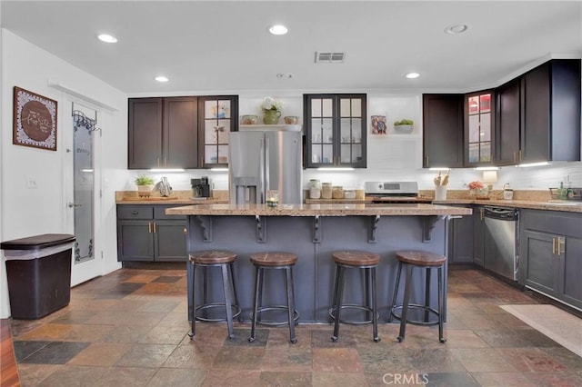kitchen with open shelves, stainless steel appliances, visible vents, light stone countertops, and glass insert cabinets