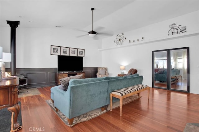 living area with a wainscoted wall, a ceiling fan, wood finished floors, a wood stove, and visible vents
