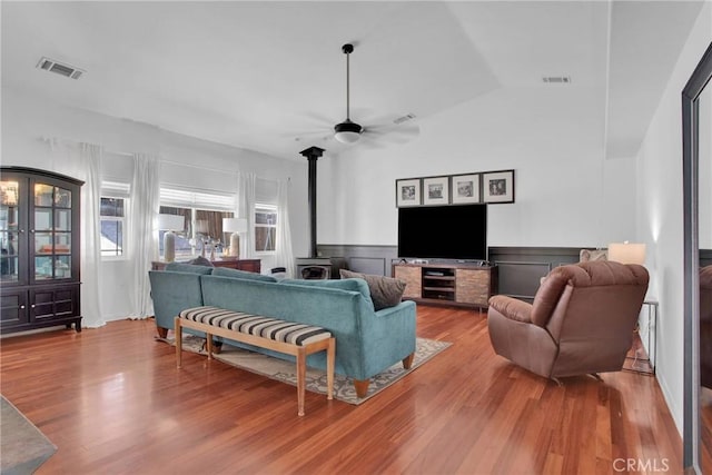 living area featuring ceiling fan, wood finished floors, a wood stove, and visible vents