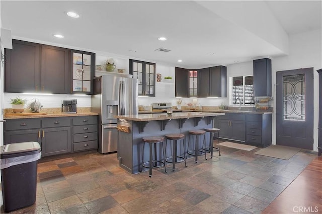 7575 Rancho Rd, Wrightwood, CA 92372 - kitchen with stainless steel fridge, a kitchen bar, glass insert cabinets, recessed lighting, and stone tile floors