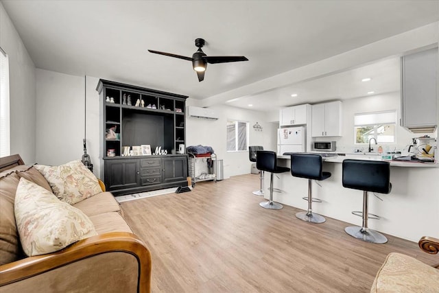 living area featuring a ceiling fan, light wood-type flooring, an AC wall unit, and recessed lighting