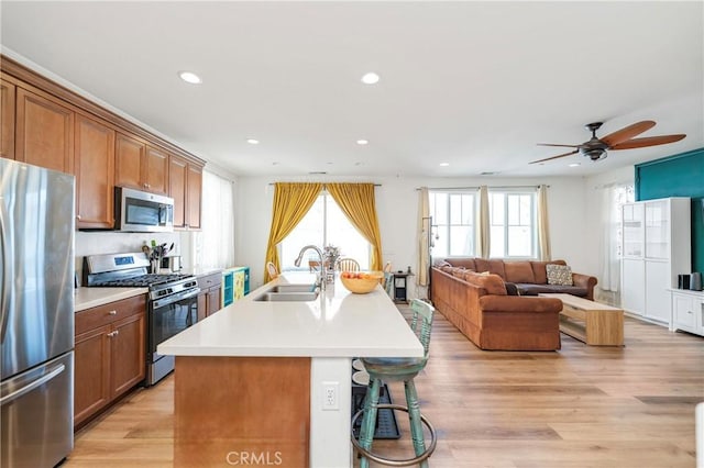 kitchen with light wood-style flooring, appliances with stainless steel finishes, brown cabinets, and a sink