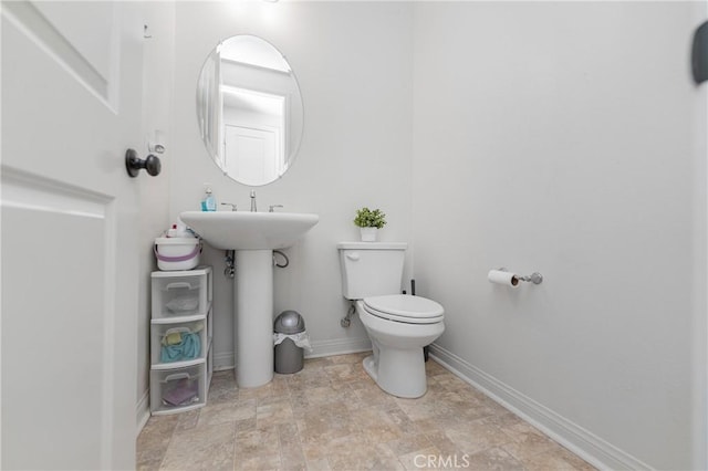 half bathroom with toilet, stone finish floor, and baseboards