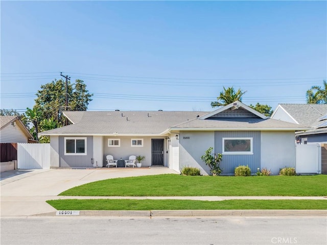 ranch-style home featuring concrete driveway, a front lawn, a patio area, and fence