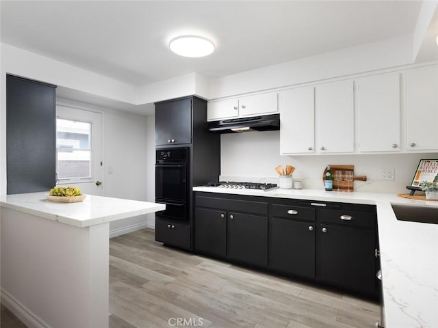 kitchen featuring gas cooktop, under cabinet range hood, white cabinetry, black oven, and light wood finished floors