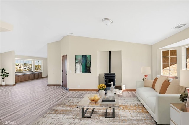 living area with visible vents, baseboards, wood finished floors, a wood stove, and vaulted ceiling