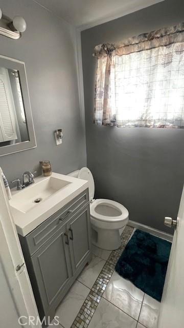 half bathroom with toilet, marble finish floor, and vanity