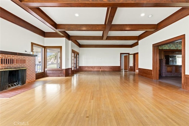 unfurnished living room featuring coffered ceiling, a wainscoted wall, beamed ceiling, wood finished floors, and a fireplace