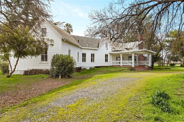 back of property with driveway, covered porch, a chimney, and a lawn