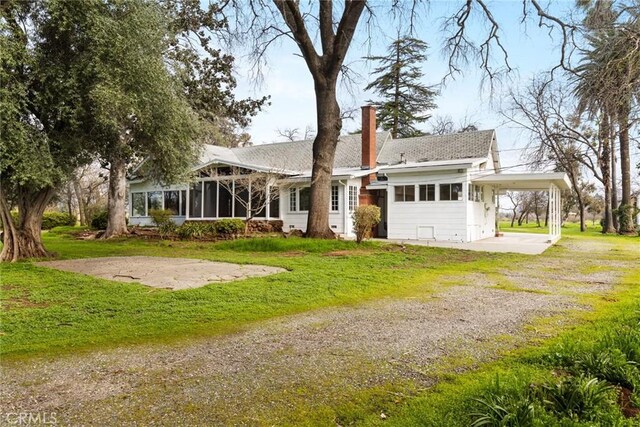 view of front facade featuring driveway, a chimney, a front yard, and a sunroom