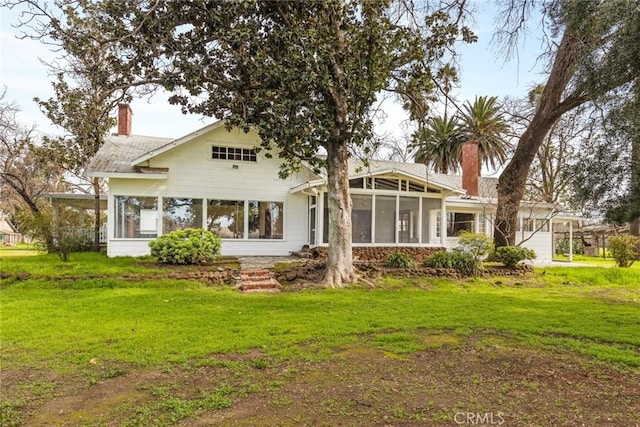 rear view of house featuring a lawn, a chimney, and a sunroom