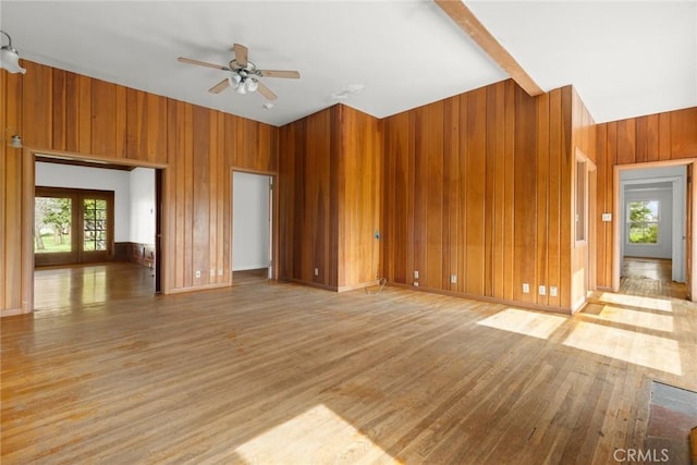 unfurnished living room featuring french doors, light wood finished floors, a towering ceiling, ceiling fan, and wooden walls