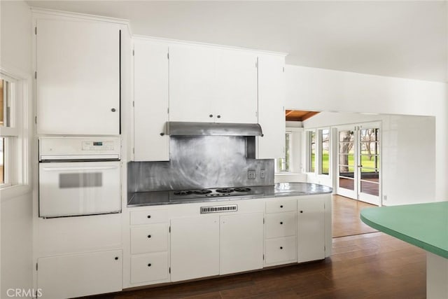 kitchen featuring oven, under cabinet range hood, dark wood-style flooring, white cabinetry, and backsplash