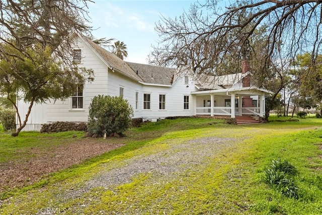 rear view of house with driveway, covered porch, a chimney, and a yard