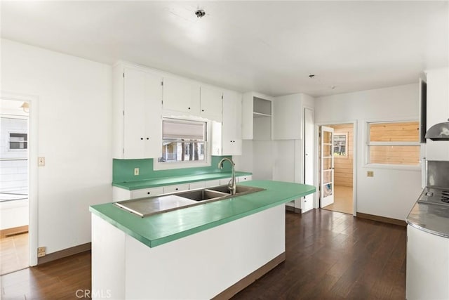 kitchen with baseboards, white cabinets, an island with sink, dark wood-type flooring, and a sink