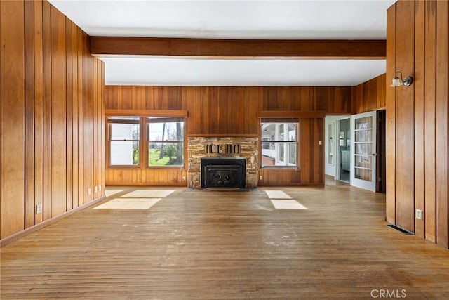 unfurnished living room with a fireplace with flush hearth, beamed ceiling, wood finished floors, and wooden walls