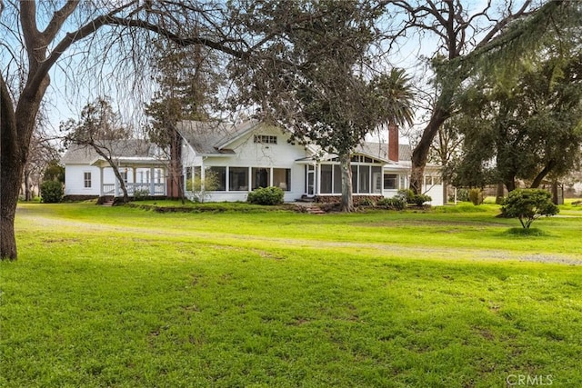 exterior space with a sunroom, a yard, a chimney, and an attached garage