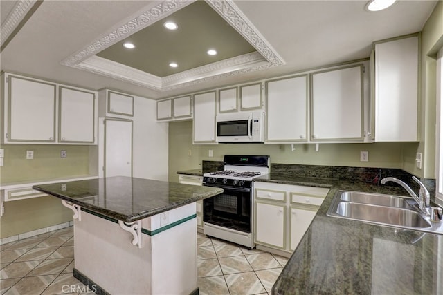 kitchen featuring range with gas stovetop, a tray ceiling, white microwave, white cabinets, and a sink